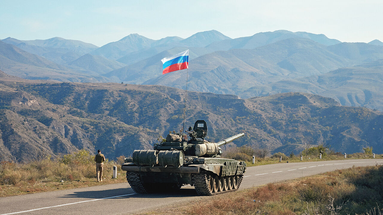 A service member of the Russian peacekeeping troops walks by a tank near the border with Armenia