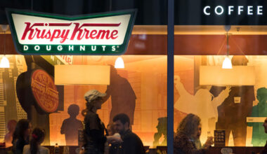 Exterior of Krispy Kreme doughnut store with customers sitting inside.