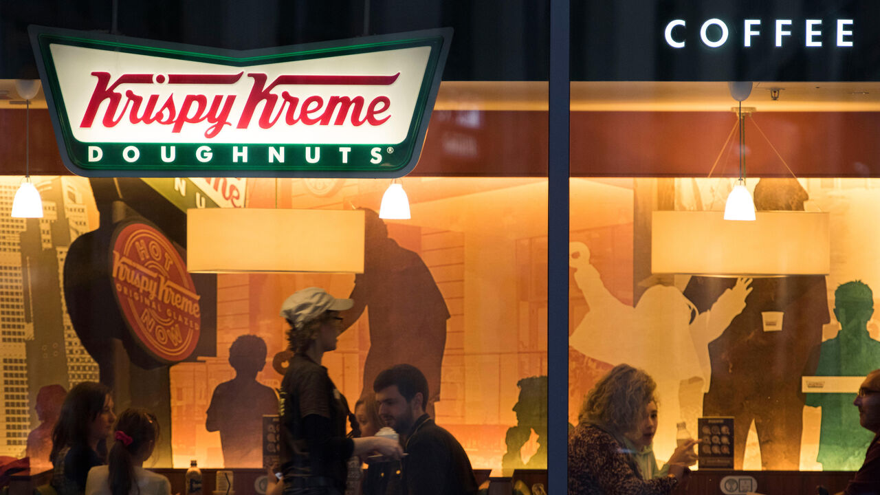 Exterior of Krispy Kreme doughnut store with customers sitting inside.