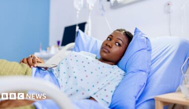 Young lady in hospital gown in hospital bed looking pensive.