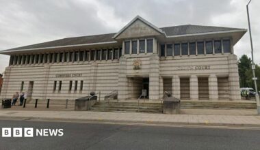 A large white stone building with steps going up to it, it has several pillars and a row of rectangular windows at the top.