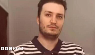 A man with dark hair wearing a black and white T-shirt.