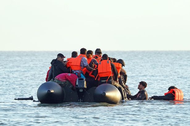 A group of people thought to be migrants wade through the sea to clamber aboard a small boat off the beach