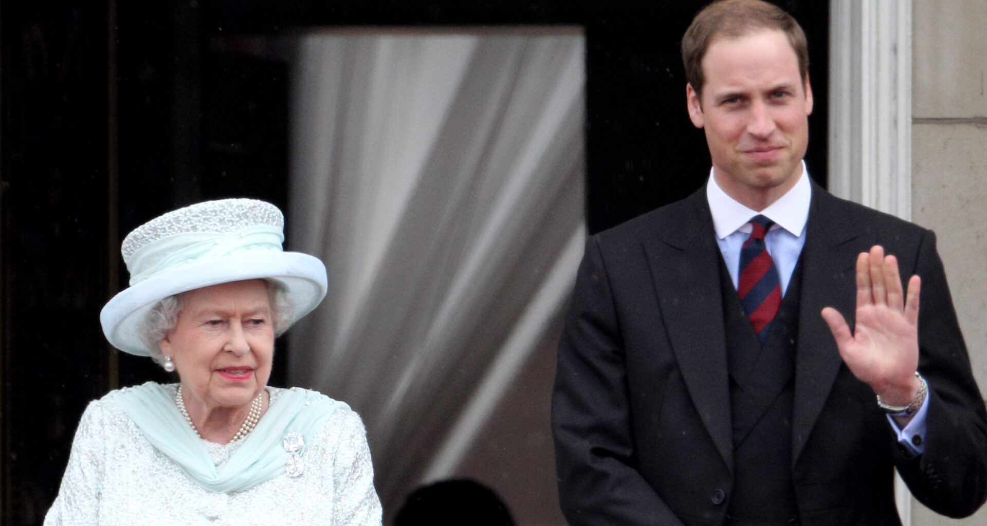 Queen Elizabeth II wears a blue jacket and matching hat and Prince William wears a suit