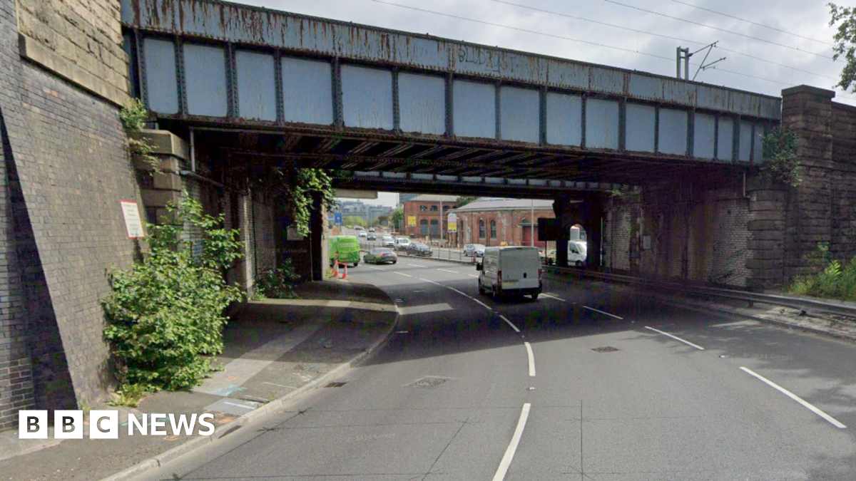 A three-lane road leading under a pair of railway bridges