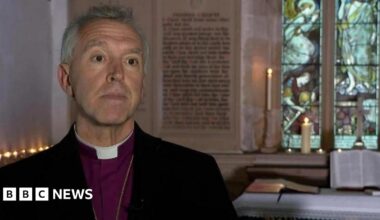 Former Archbishop of Wales, The Most Reverend, Andrew John. He is on the left of the image and has short grey hair. He has a black jacket on, purple shirt and a white dog collar.