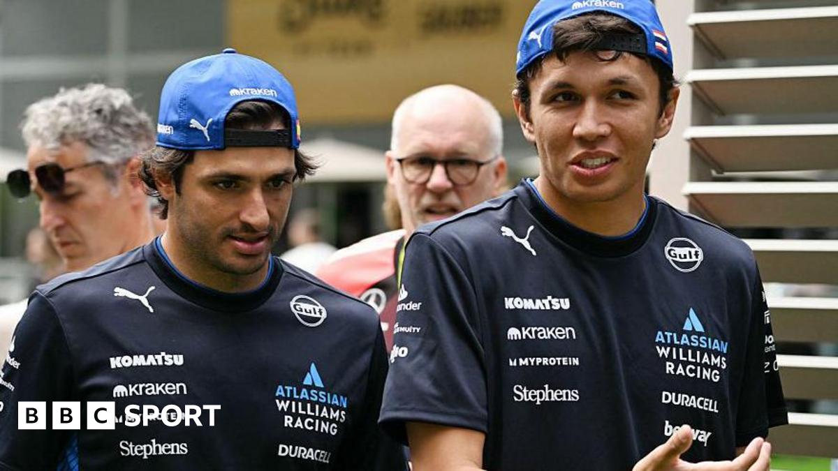 Carlos Sainz and Alex Albon in conversation at the Miami Grand Prix. Both men are wearing Williams t-shirts and caps back to front