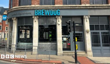 The outside of a Brewdog pub on a street corner. The company's name is in blue letters above the pub entrance. Traffic lights and other street furniture can be seen.