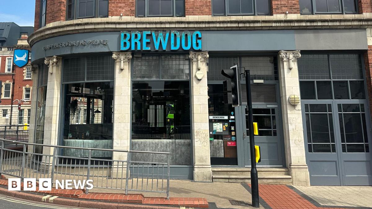 The outside of a Brewdog pub on a street corner. The company's name is in blue letters above the pub entrance. Traffic lights and other street furniture can be seen.