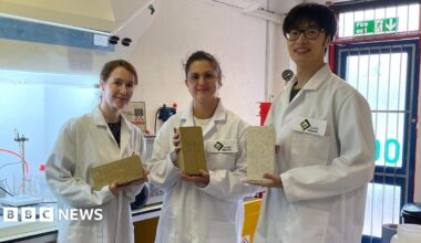 Three members of the earth4Earth company, wearing white lab coats, in their research facility at Sheffield Technology Parks. They each hold one of the "carbon absorbing" bricks. Two of the bricks are beige in colour and the other brick is an off-white colour.