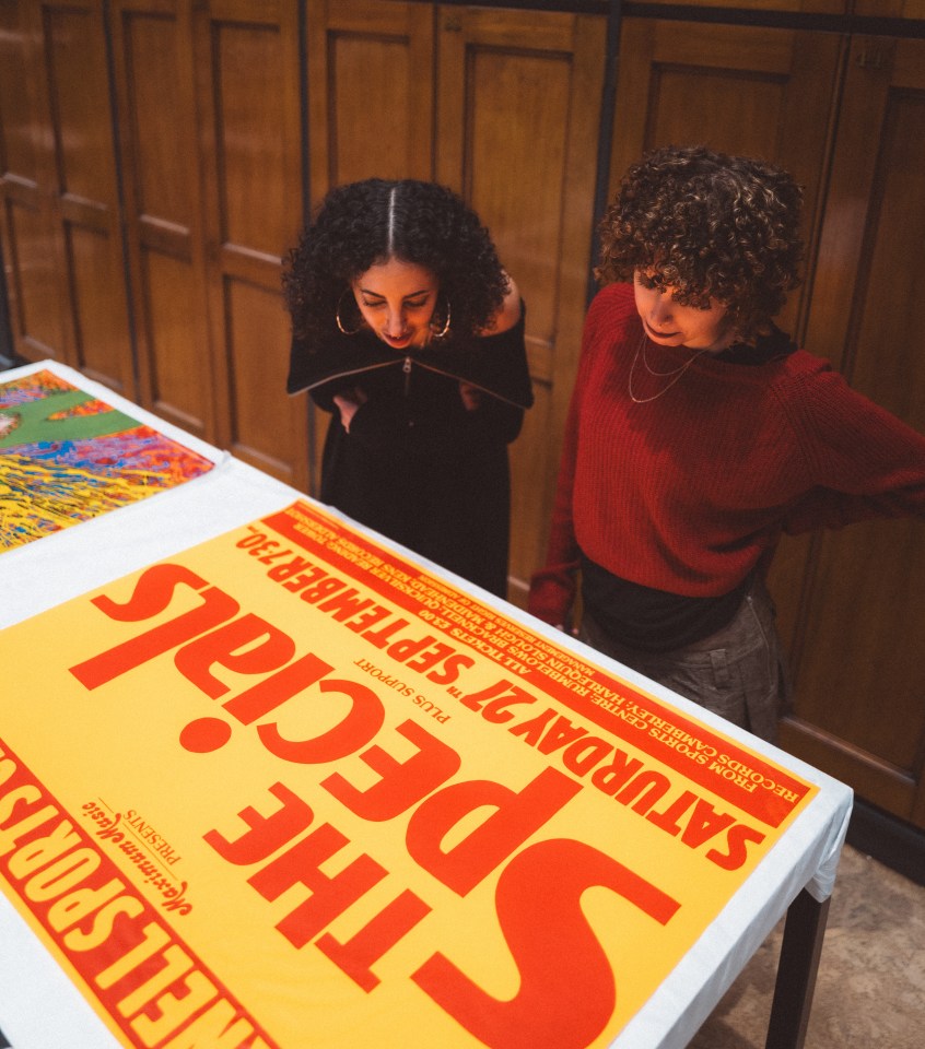 Two people looking at a poster for "The Specials" concert.