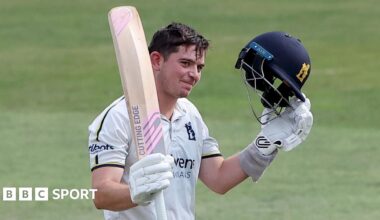 Ethan Bamber raises his bat and helmet to celebrate his century for Warwickshire