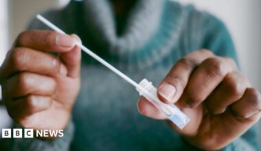 Anonymous shot of a person wearing a green polo neck jumper and holding a plastic test tube and a pipette.