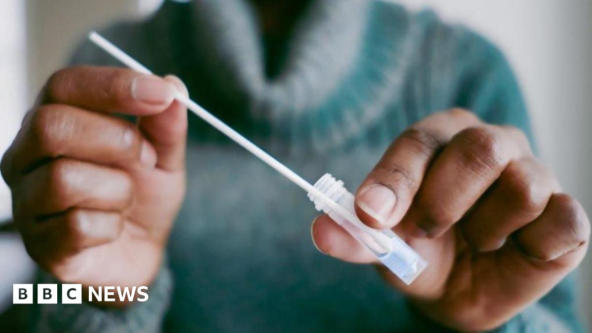 Anonymous shot of a person wearing a green polo neck jumper and holding a plastic test tube and a pipette.