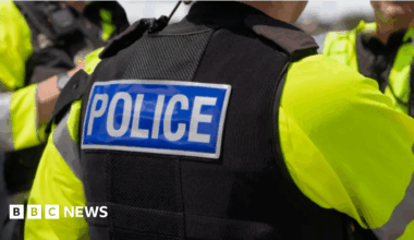 Shows police officers in flak jackets and yellow bibs