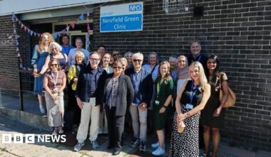 A photo of members of staff gathered outside the Newfield Green Clinic, which has a colourful banner draped around its entrance.
