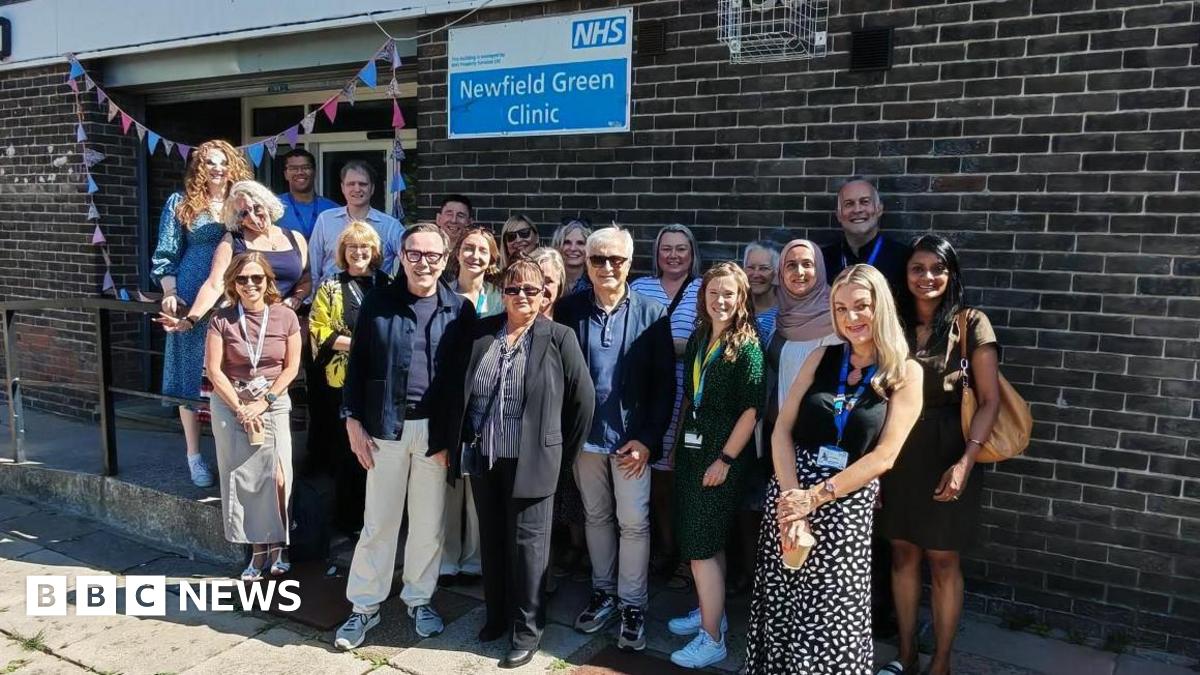 A photo of members of staff gathered outside the Newfield Green Clinic, which has a colourful banner draped around its entrance.