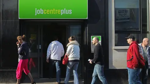 Getty Images five people queue up to enter a job centre, while another woman walks past the front door