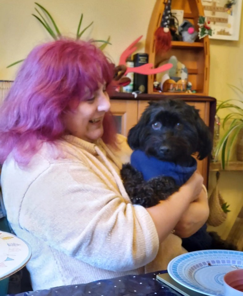 Woman with pink hair holding a small black dog.