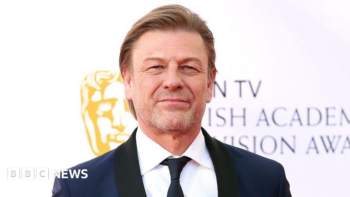 Close-up image of Sean Bean looking into the camera, wearing a dark blue and black tuxedo and black tie.