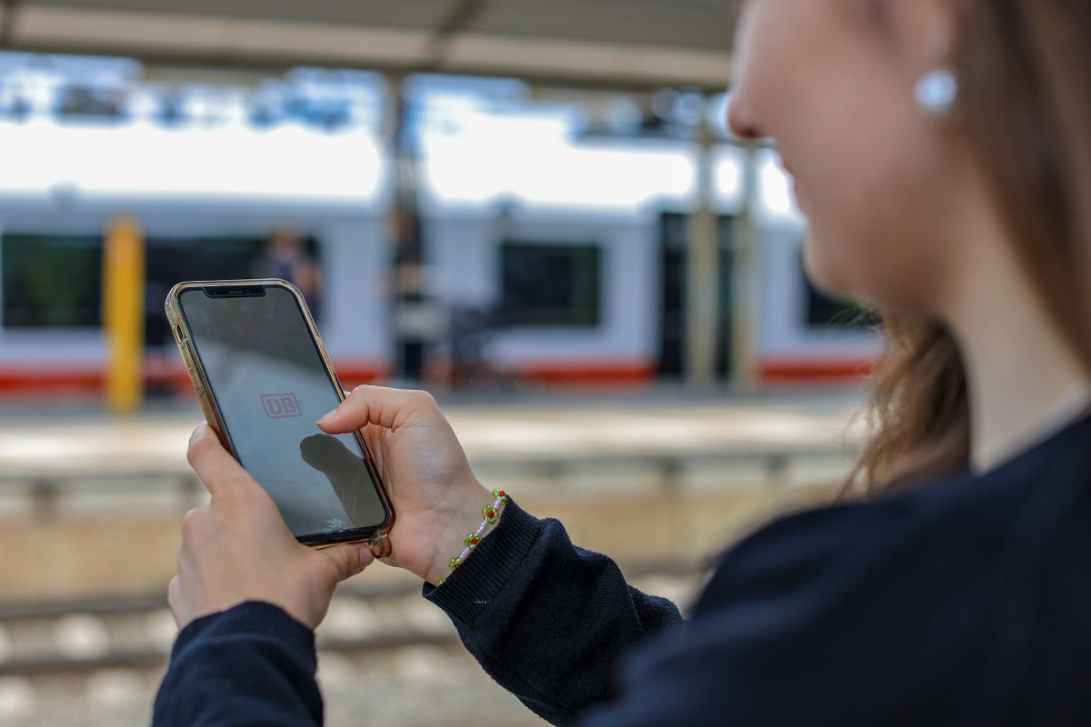 A woman holds up her phone with the DB navigator app opening on the screen.