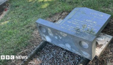 A knocked-over tomb stone bearing the name Caroline Grayson in a grassed cemetery.