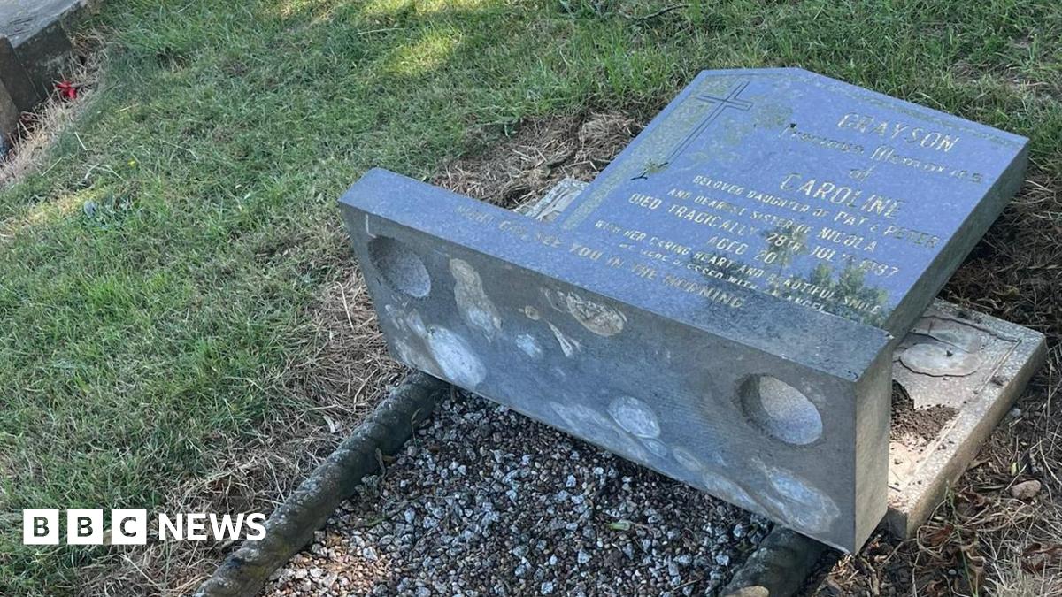 A knocked-over tomb stone bearing the name Caroline Grayson in a grassed cemetery.