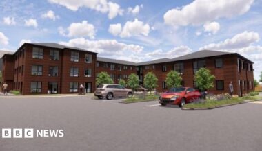 A CGI image showing a building with three floors in some parts and two floors in others. it has lots of windows and ample parking. Small trees line the outskirts of the block and there are areas of grass and flowers.