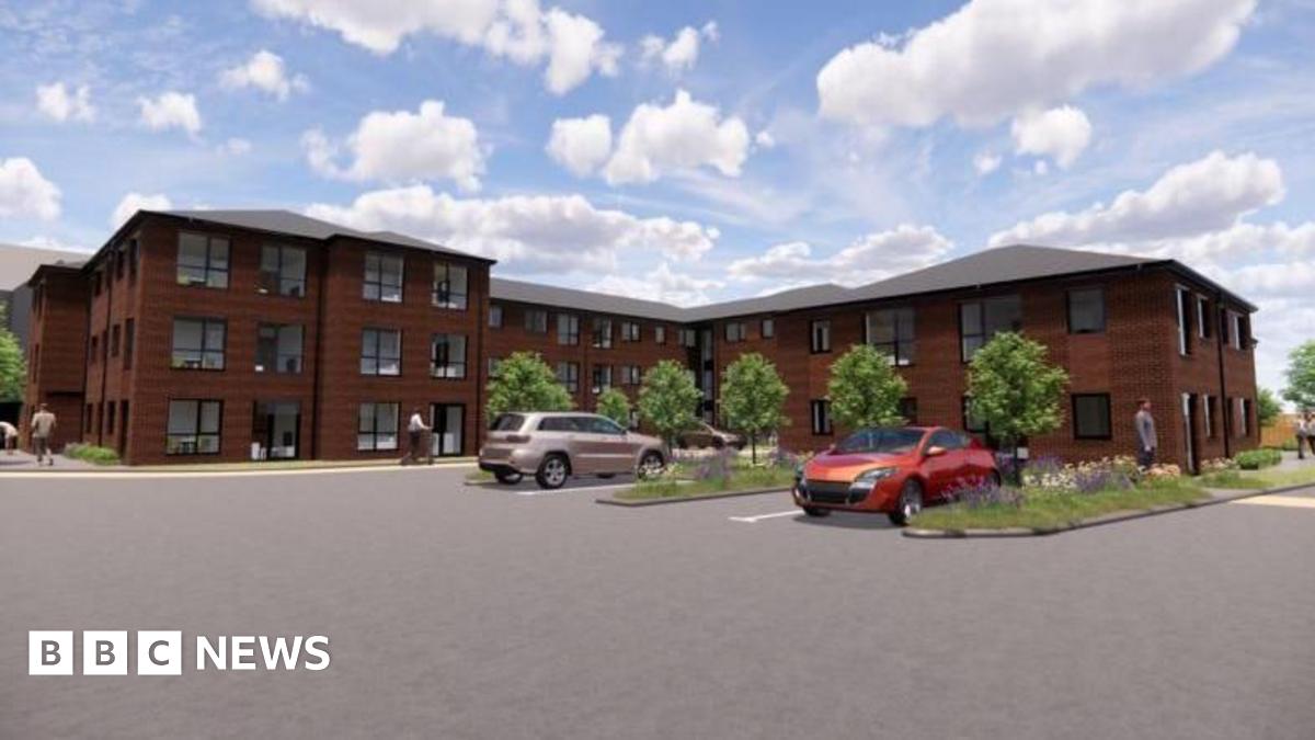 A CGI image showing a building with three floors in some parts and two floors in others. it has lots of windows and ample parking. Small trees line the outskirts of the block and there are areas of grass and flowers.