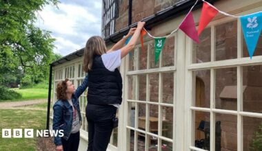 Two women putting up National Trust bunting on the outside of a house