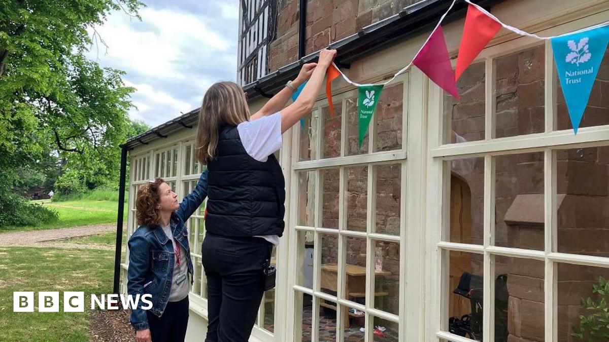 Two women putting up National Trust bunting on the outside of a house