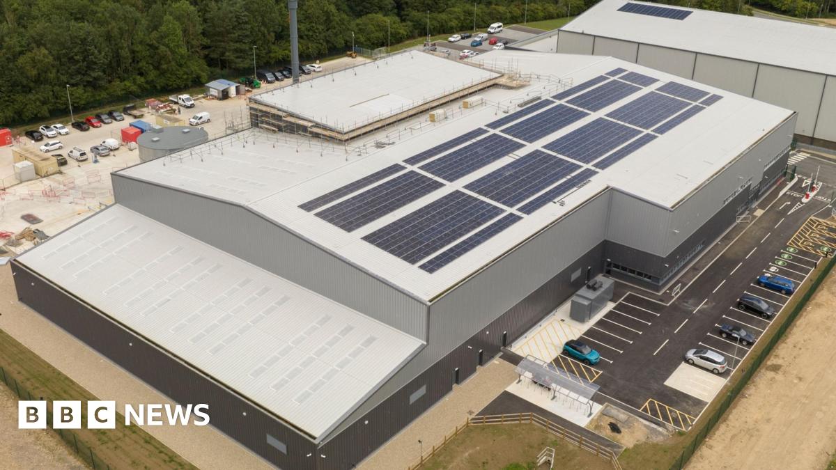 An aerial view of a large grey and black facility with car parks on both sides of the building.