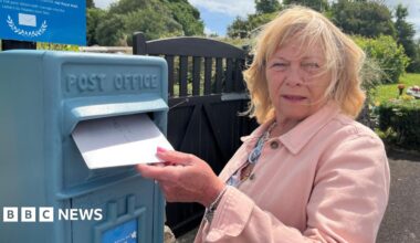 A woman posts a letter in a bright blue postbox