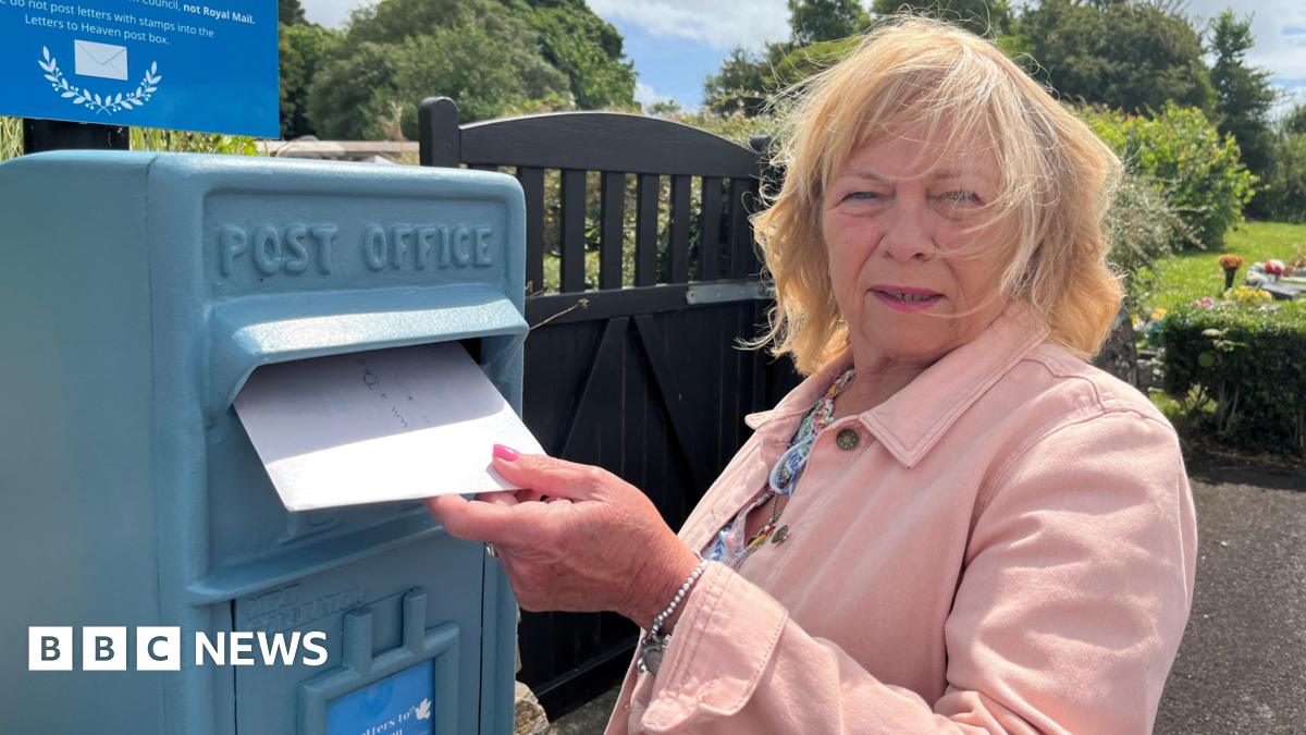 A woman posts a letter in a bright blue postbox