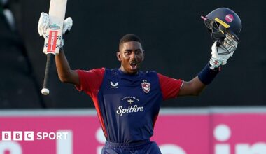 Tawanda Muyeye raises his helmet and bat in each arm in celebration