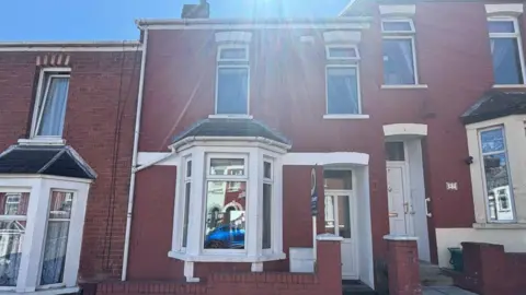 Sarah Lawrence Photograph of a red brick terraced house for sale on Trinity Street, Barry Island. The door is white and the windows have white painted frames around them. 