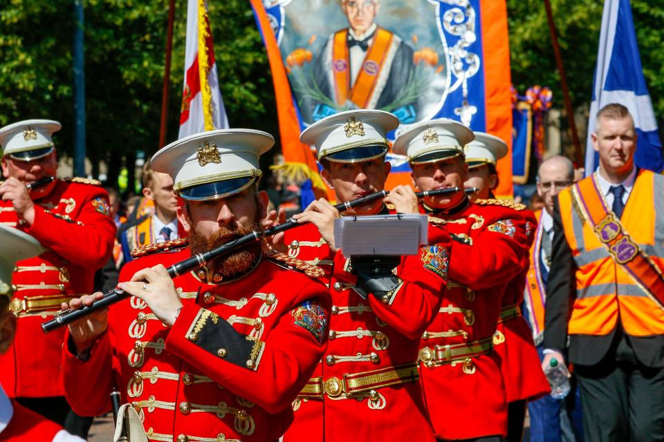Loyal Orange Lodge members in red uniforms playing flutes in a parade.