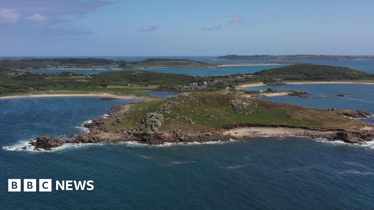 The island of Bryher is shown with rocky hills, sandy beaches and bodies of water beneath a blue sky scattered with clouds.