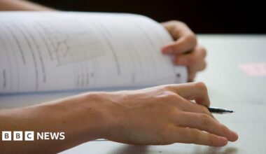 A student opens an exam paper with pen in hand. Only their hands are visible beyond the pen and paper.