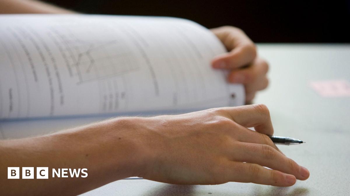 A student opens an exam paper with pen in hand. Only their hands are visible beyond the pen and paper.