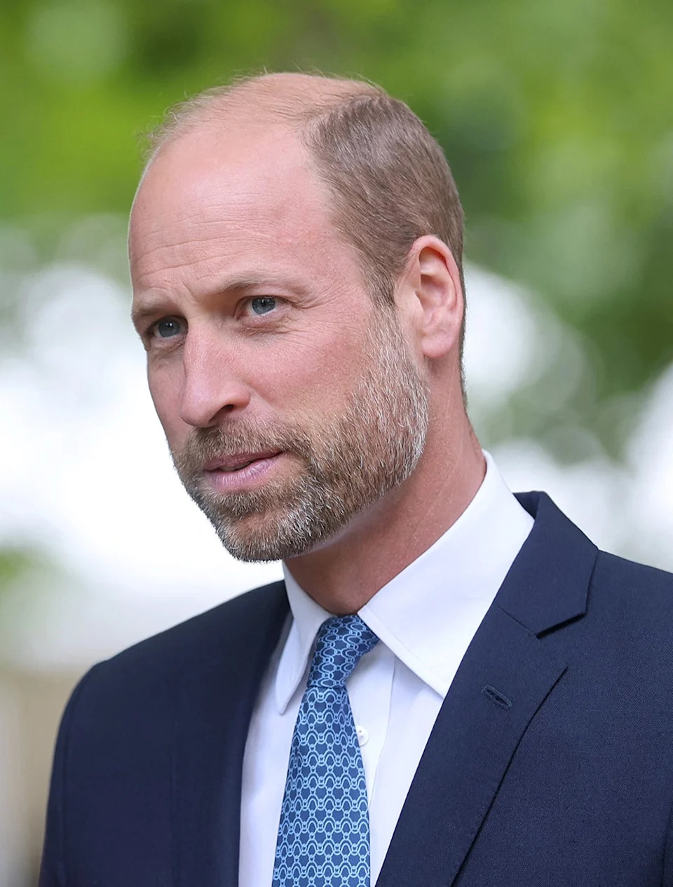 A close-up of Prince William in a dark blue suit with a light blue tie.