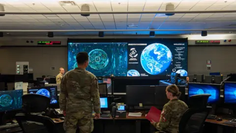 BBC/Matthew Goddard Space Force units looking at monitors in their base, showing the planet and things currently orbiting it