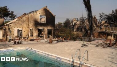 A burned house, which is missing its windows and roof, is seen surrounded by piles of debris