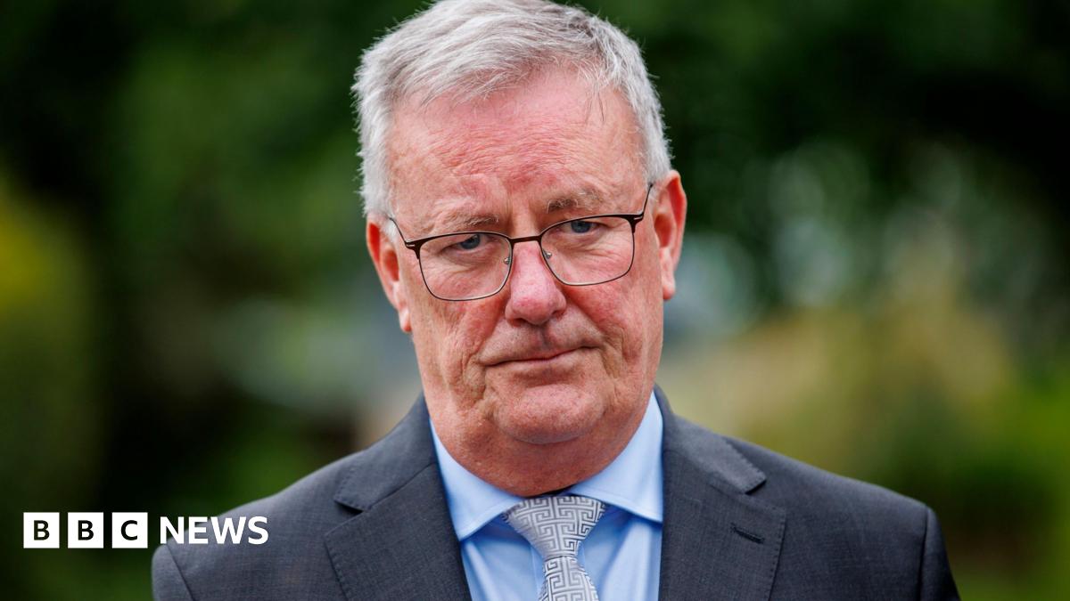 Mike Nesbitt, he has grey hair and is wearing glasses and a grey suit jacket over a blue shirt and silver tie.