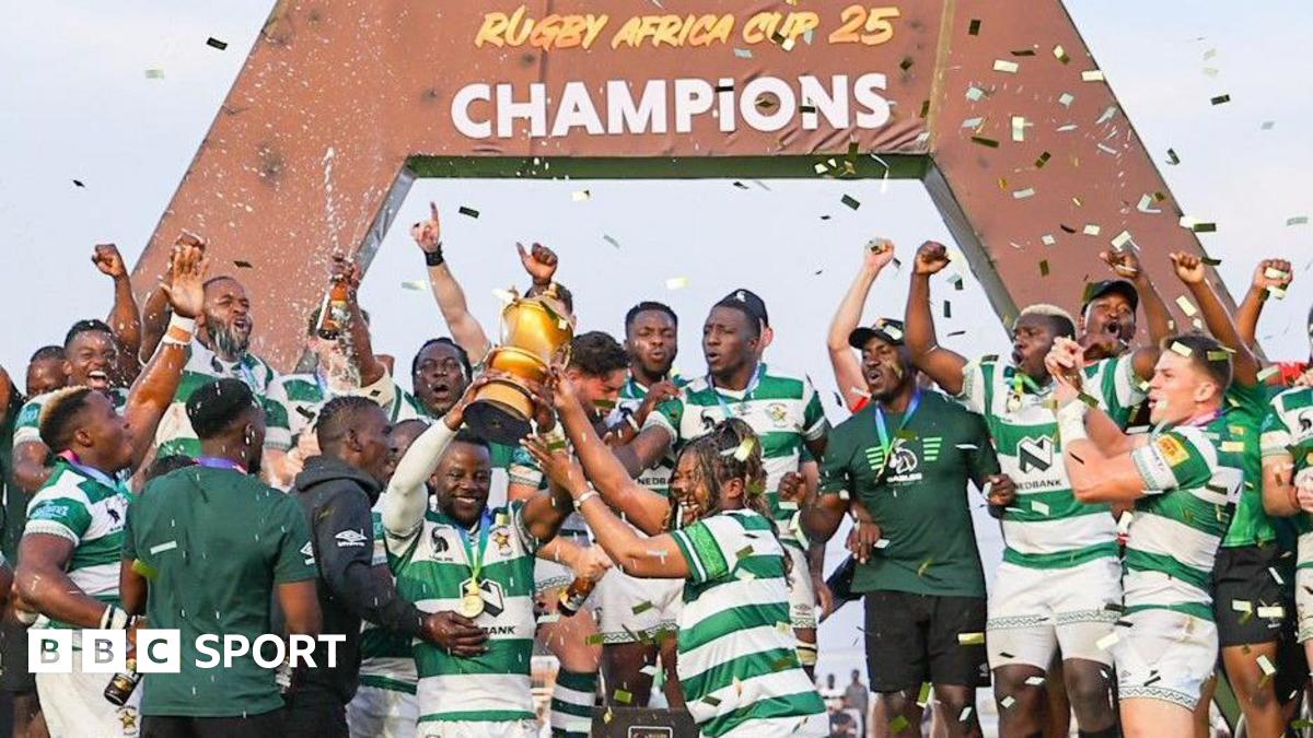 Zimbabwe's rugby players dressed in green and white lift a golden trophy and celebrate in front of a sign that says Rugby Africa Cup 25 champions