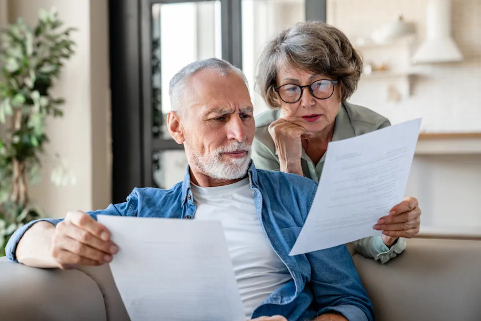 An older man and an older woman look puzzled while reading a document.