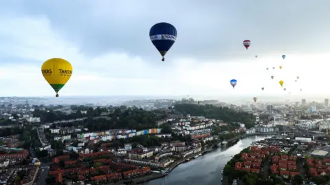 Reuters A wide shot image showing many hot air balloons flying over Bristol. The city landscape can be seen in the distance. 