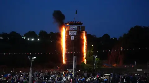 PA Media A wide shot of the whole bonfire, flames are up the side of it. It's dark but the outline of the bonfire can be seen. 