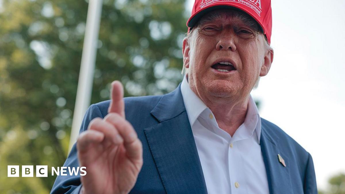 Donald Trump wearing a white shirt and navy suit jacket with no tie. He is wearing a red cap which bears the words: GULF OF AMERICA. Yet another TRUMP development.