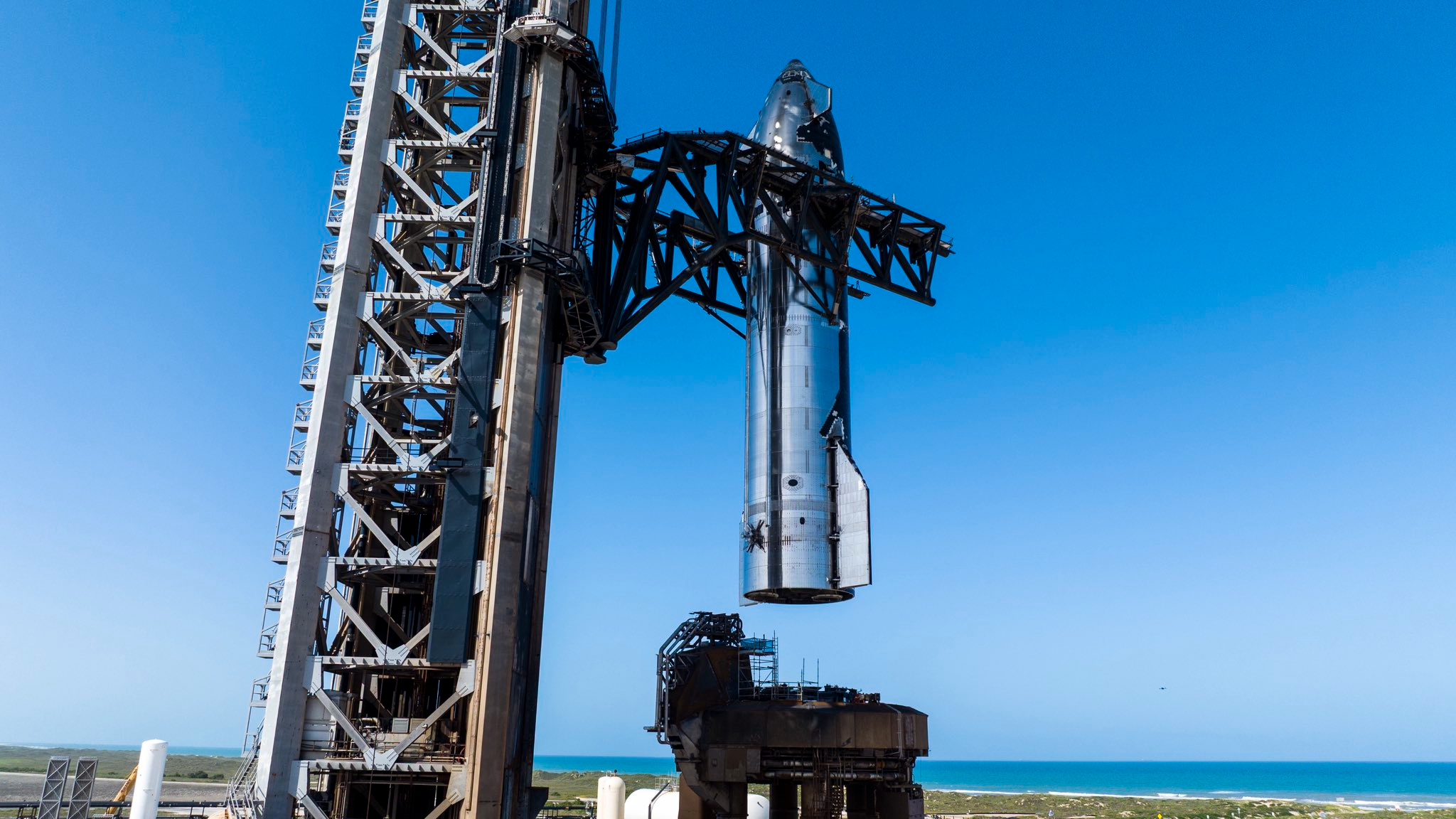 a large silver rocket is lifted onto a launch mount at a seaside pad